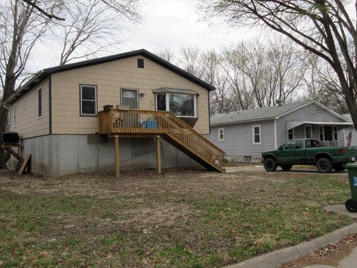A home has been elevated on solid perimeter walls. The elevation is constructed of cast-in-place concrete. Also visible are the new staircase for building access and elevated utilities against the side of the house.
