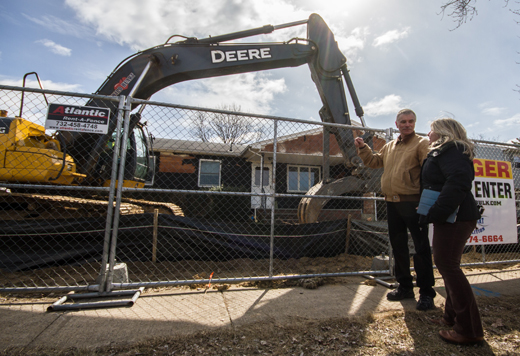 Two individuals standing outside a construction fence around a home and hydraulic excavator.